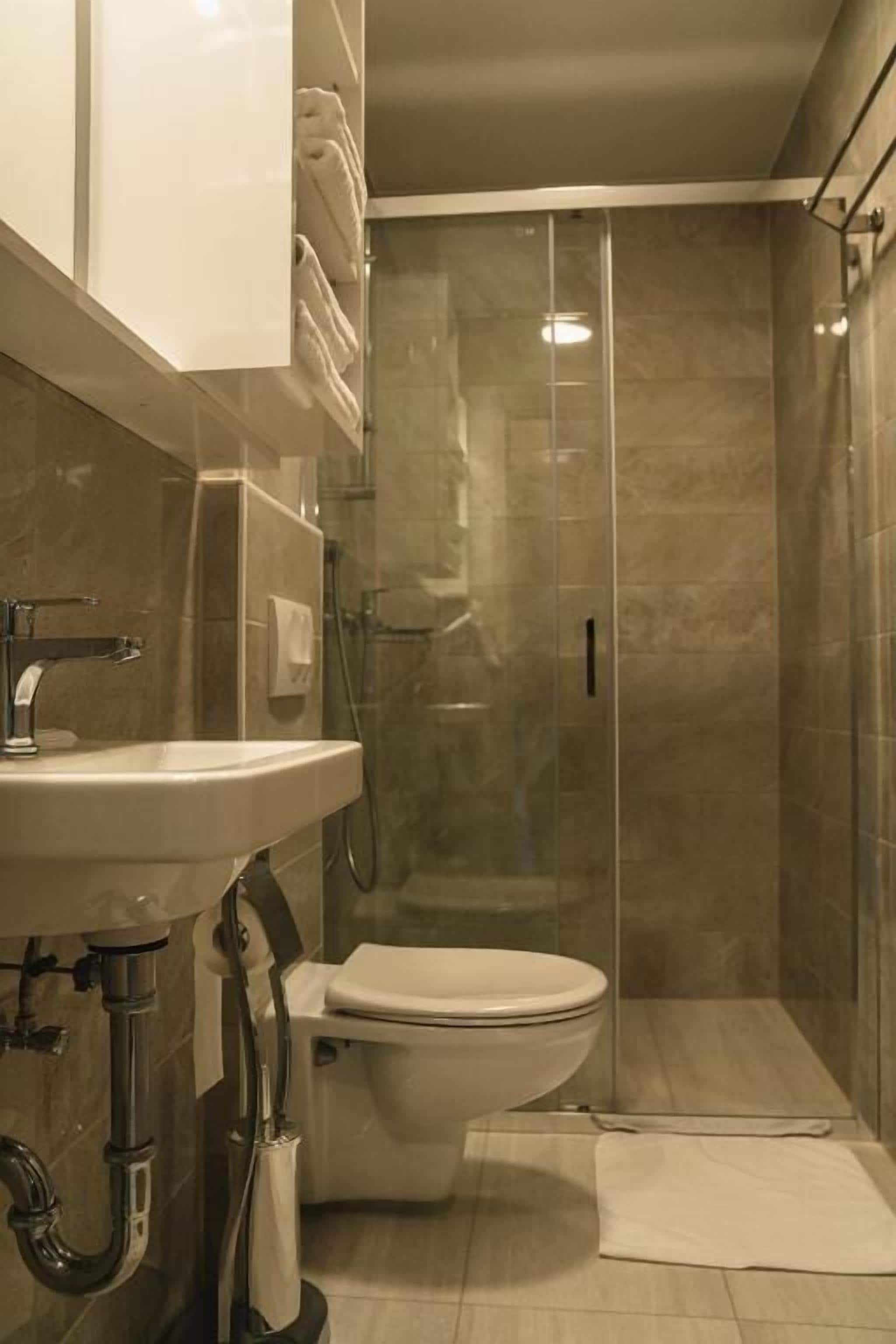 Un baño moderno con cabina de ducha acristalada, un lavamanos blanco y un inodoro.