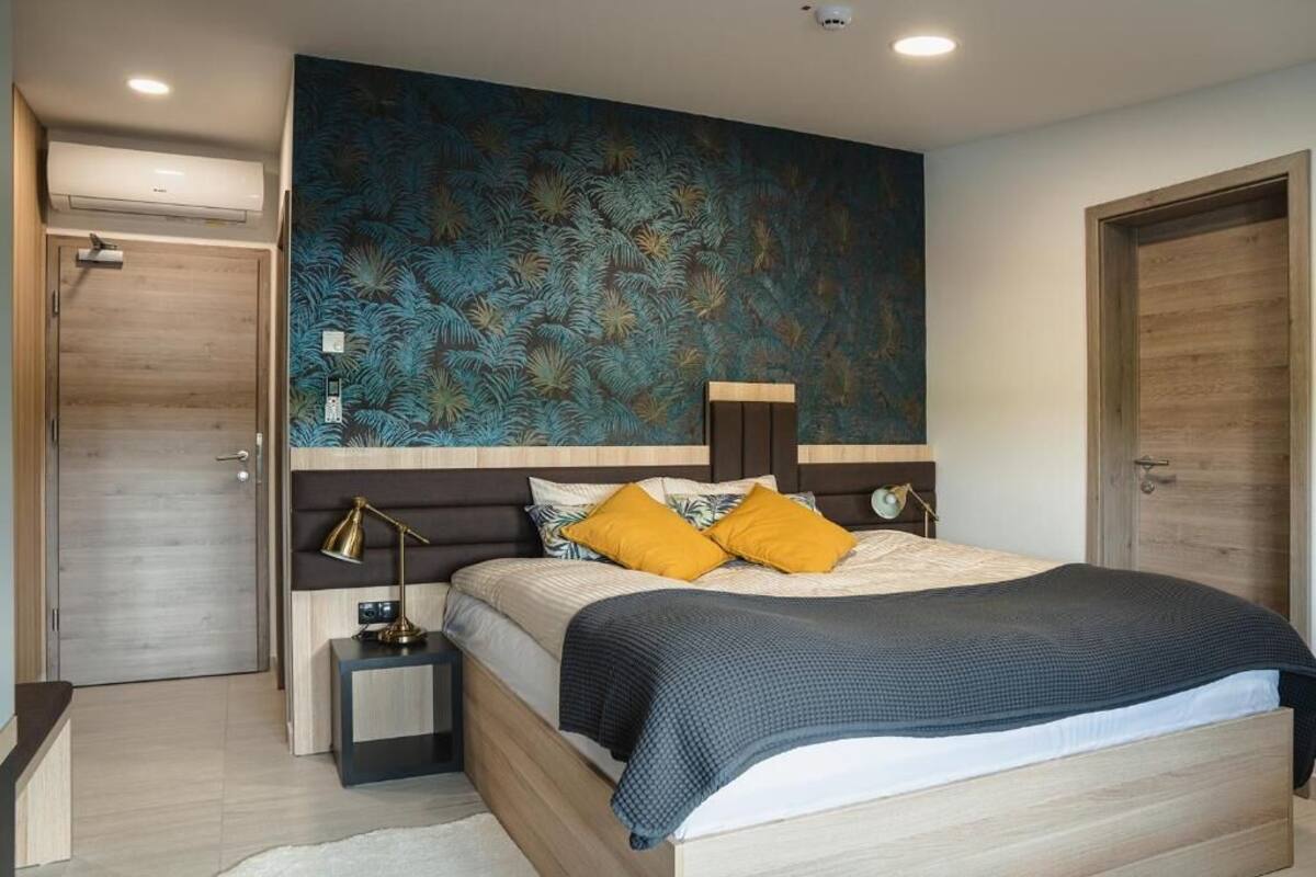 A modern bedroom with a large bed, a nightstand, a wall-mounted lamp, and a door.