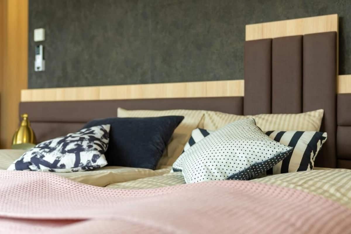 A hotel room with a bed featuring multiple pillows and a headboard with a wooden and fabric design.
