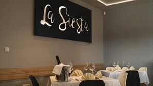 A restaurant interior with tables set for dining, a wall sign reading "La Siesta", and a modern design with wooden accents. - La Siesta (Markovci)