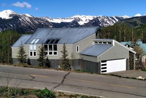 A two-story building with a garage, a sloped roof, and a view of snow-capped mountains. - Anthracite Allure 4 BR, ski in/out, pet friendly, hottub (Mt. Crested Butte)