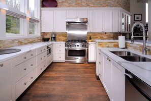 A modern kitchen with white cabinets, a stainless steel stove, and a wooden floor. - Anthracite Allure 4 BR, ski in/out, pet friendly, hottub (Mt. Crested Butte)