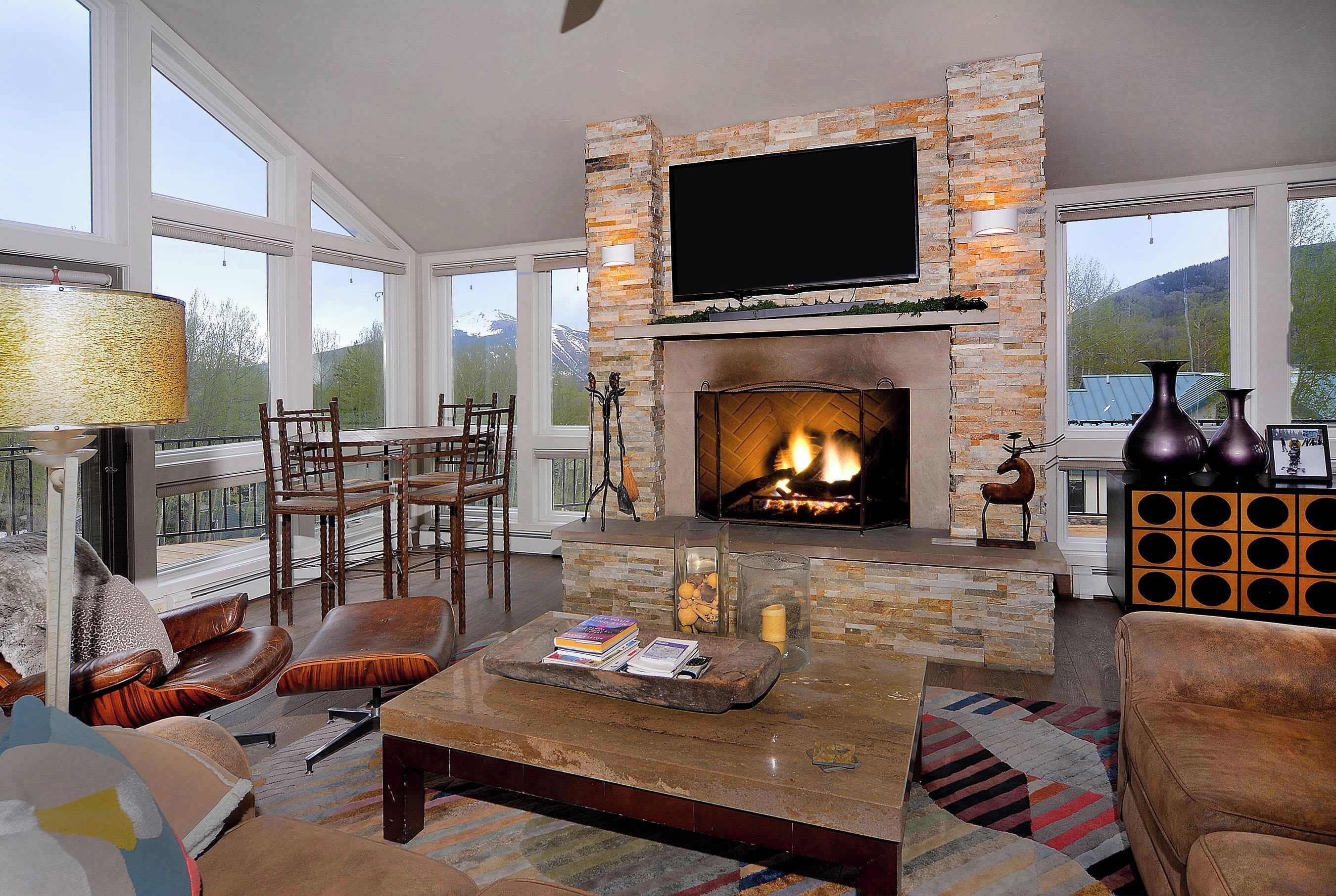 A spacious living room with a stone fireplace, a flat-screen TV mounted above it, and a comfortable seating area with leather sofas and chairs.