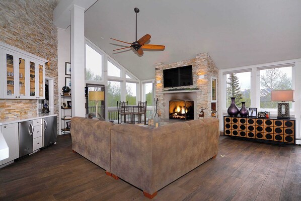 A spacious living area with a fireplace, a ceiling fan, and a television mounted on a stone wall. - Anthracite Allure 4 BR, ski in/out, pet friendly, hottub (Mt. Crested Butte)