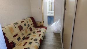Ein schmaler Flur mit einem beigen Sofa mit Muster und einer Tür zu einem Badezimmer mit Spiegel und Waschbecken.