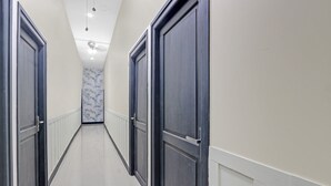 A corridor with dark wooden doors, white walls, and a tiled floor.
