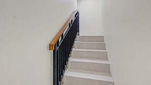 A staircase with a wooden handrail and black balusters, leading to a landing with a ceiling light.