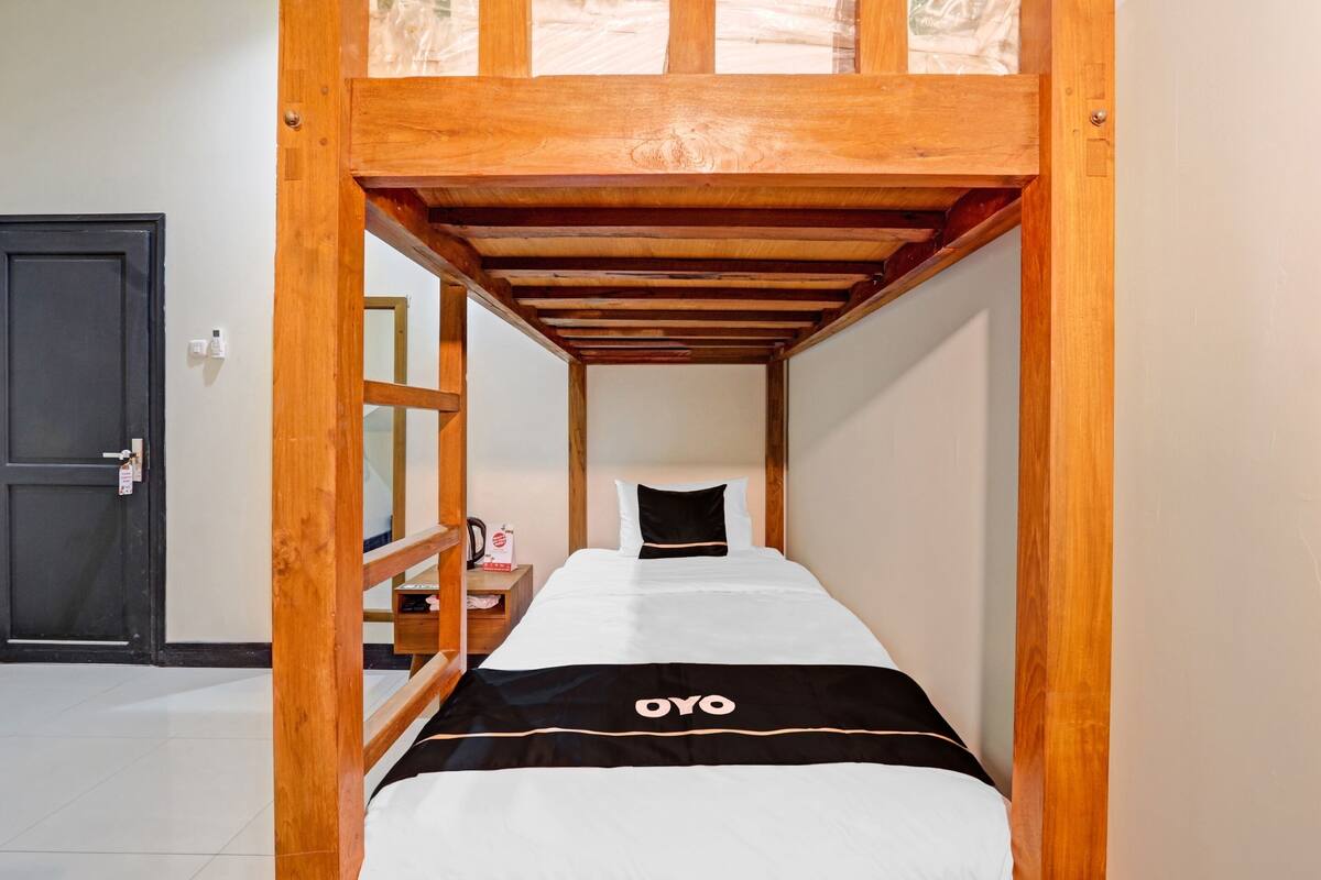 Ein Einzelzimmer mit Etagenbett, einem Holz-Kopfteil, einem Nachttisch mit Lampe und einer abschließbaren Tür.