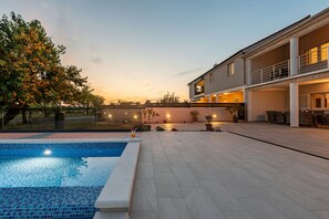 A modern house with a swimming pool, outdoor seating, and a well-lit patio area.