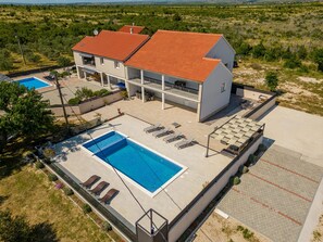A two-story building with a swimming pool, outdoor seating, and a view of the surrounding landscape.