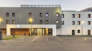 A modern hotel with a flat facade, multiple windows, and a parking lot with marked spaces. - Best Western Coeur de Maurienne Hotel Restaurant & Spa (Saint-Jean-de-Maurienne)