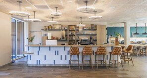 Zona de bar moderna con mostrador central, taburetes y luces colgantes.