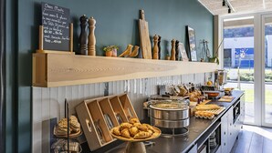 A buffet setup with various food items and utensils, a chalkboard menu, and decorative salt and pepper shakers on a shelf.