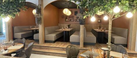 Ein Restaurant mit Sitzbänken, Tischen und hängenden Pflanzen.