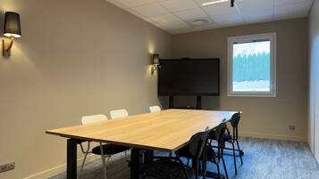 A conference room with a long table, six chairs, a flat-screen TV, and a window with a view of trees.