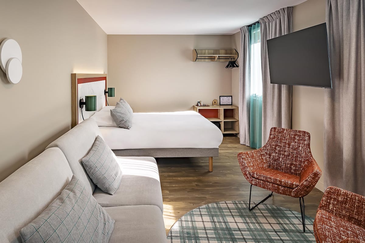 Ein Hotelzimmer mit einer Couch, einem Bett, einem Fernseher und einem Sessel.