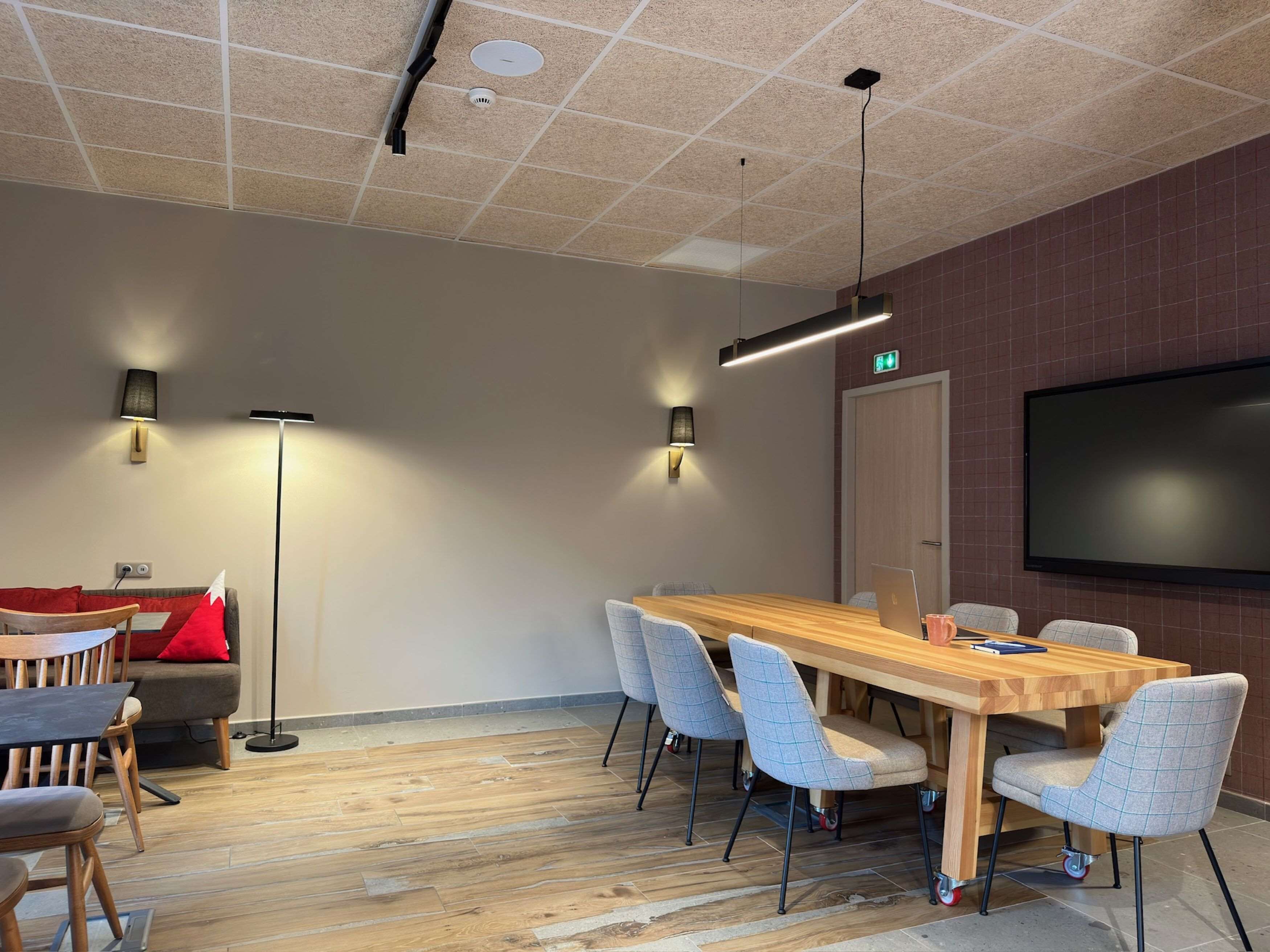 Una sala de conferencias con una larga mesa de madera, seis sillas, dos lámparas de pie, un televisor de pantalla plana y un sofá rojo.