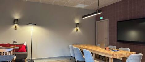 Una sala de conferencias con una larga mesa de madera, seis sillas, dos lámparas de pie, un televisor de pantalla plana y un sofá rojo.