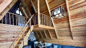 A spacious loft with a high ceiling, wooden beams, a staircase, a blue sofa, a grey armchair, and a red rug. - Sapanca Rose Garden Bungalov (Sapanca)