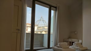 A bedroom with a bed, a desk with a lamp, and a view of buildings through a large window. - Apartment in historic villa 10 minutes from the historic center (Firenze)
