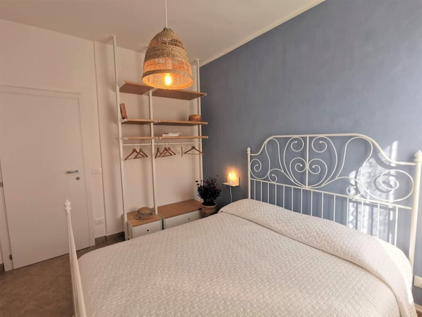 A bedroom with a bed, a hanging light fixture, a white metal headboard, and a wardrobe with shelves.
