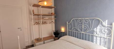 A bedroom with a bed, a hanging light fixture, a white metal headboard, and a wardrobe with shelves.