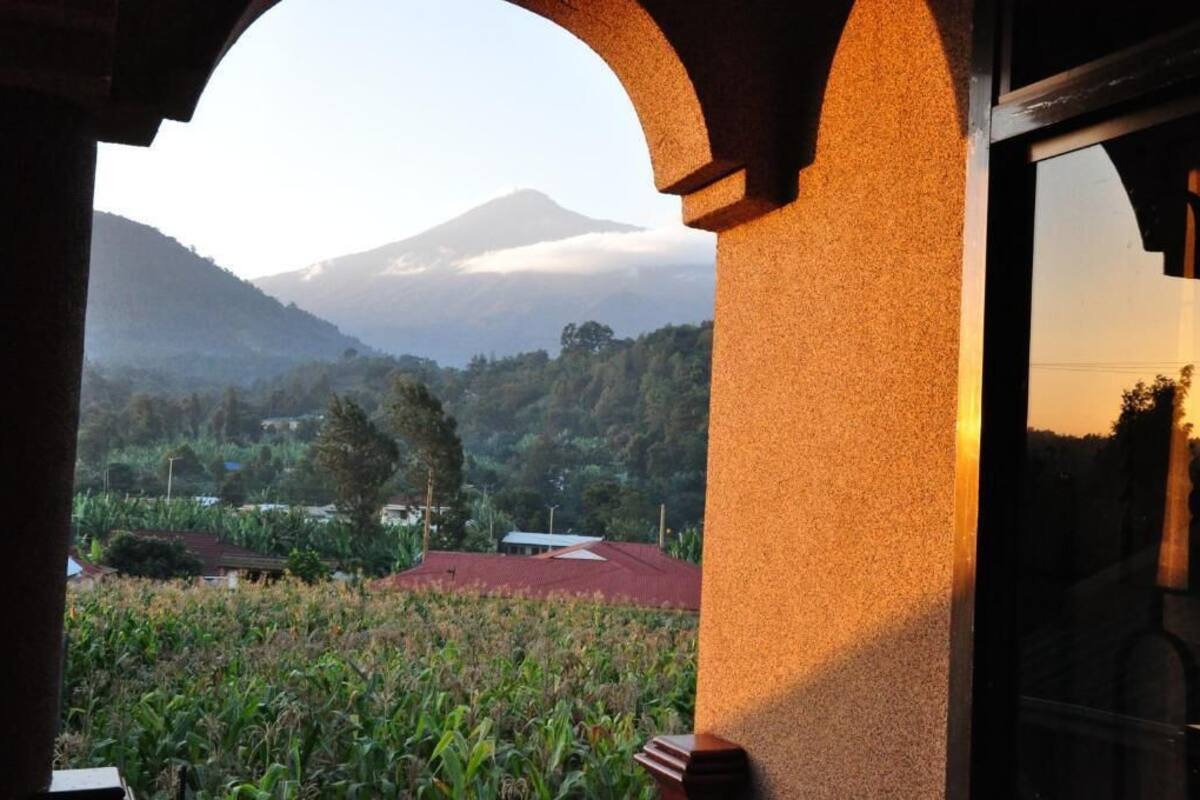 A view through an arched doorway of a rural landscape with a mountain in the background.