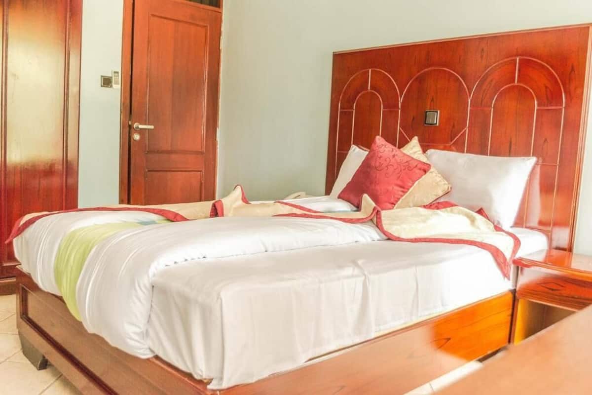 A neatly made bed with white bedding and red accents, a wooden headboard, and a wooden nightstand.