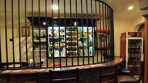 Un espace bar doté d’un comptoir incurvé, de plusieurs chaises et d’une étagère où sont exposées des bouteilles d’alcool, le tout séparé par une cloison en métal noir.