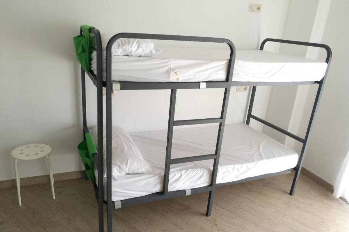 A bunk bed with two levels, a small white stool, and a green bag.