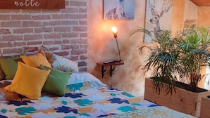 A cozy bedroom with a wooden bed, colorful pillows, a bedside plant, and artwork on the walls.