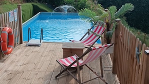 A wooden deck with a pool, two striped beach chairs, and a lifebuoy.
