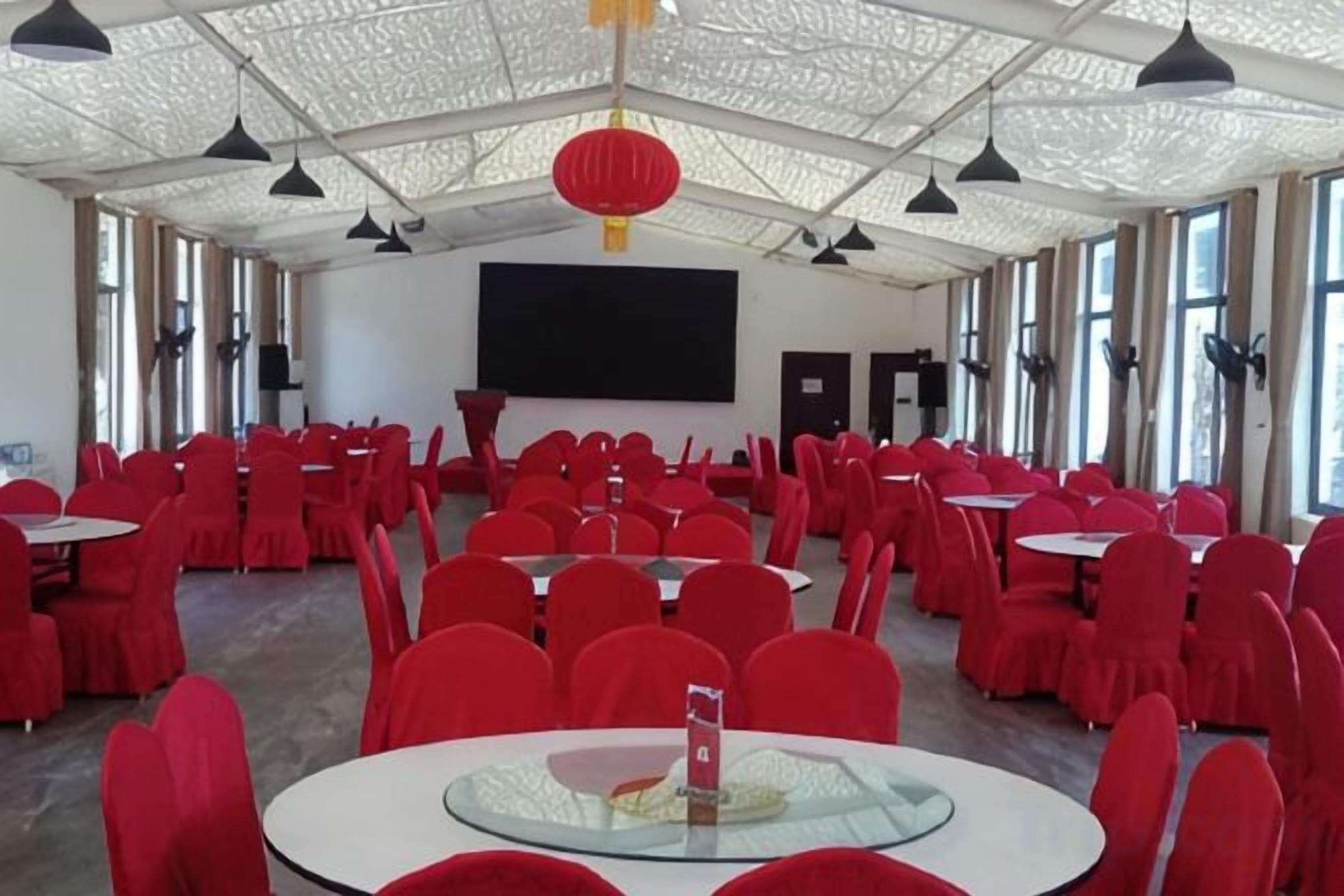 A conference room with round tables and red chairs, a large screen, and a ceiling with a patterned design.