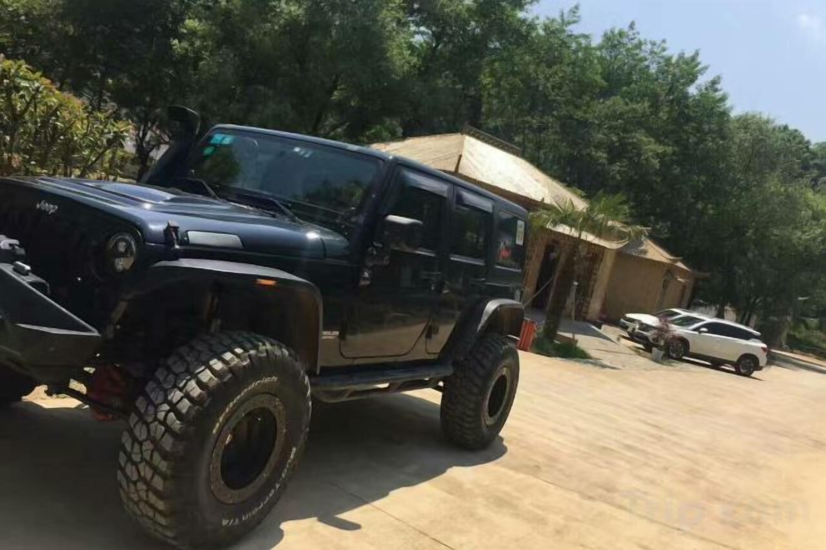 A black off-road vehicle parked in a lot with trees and a building in the background.