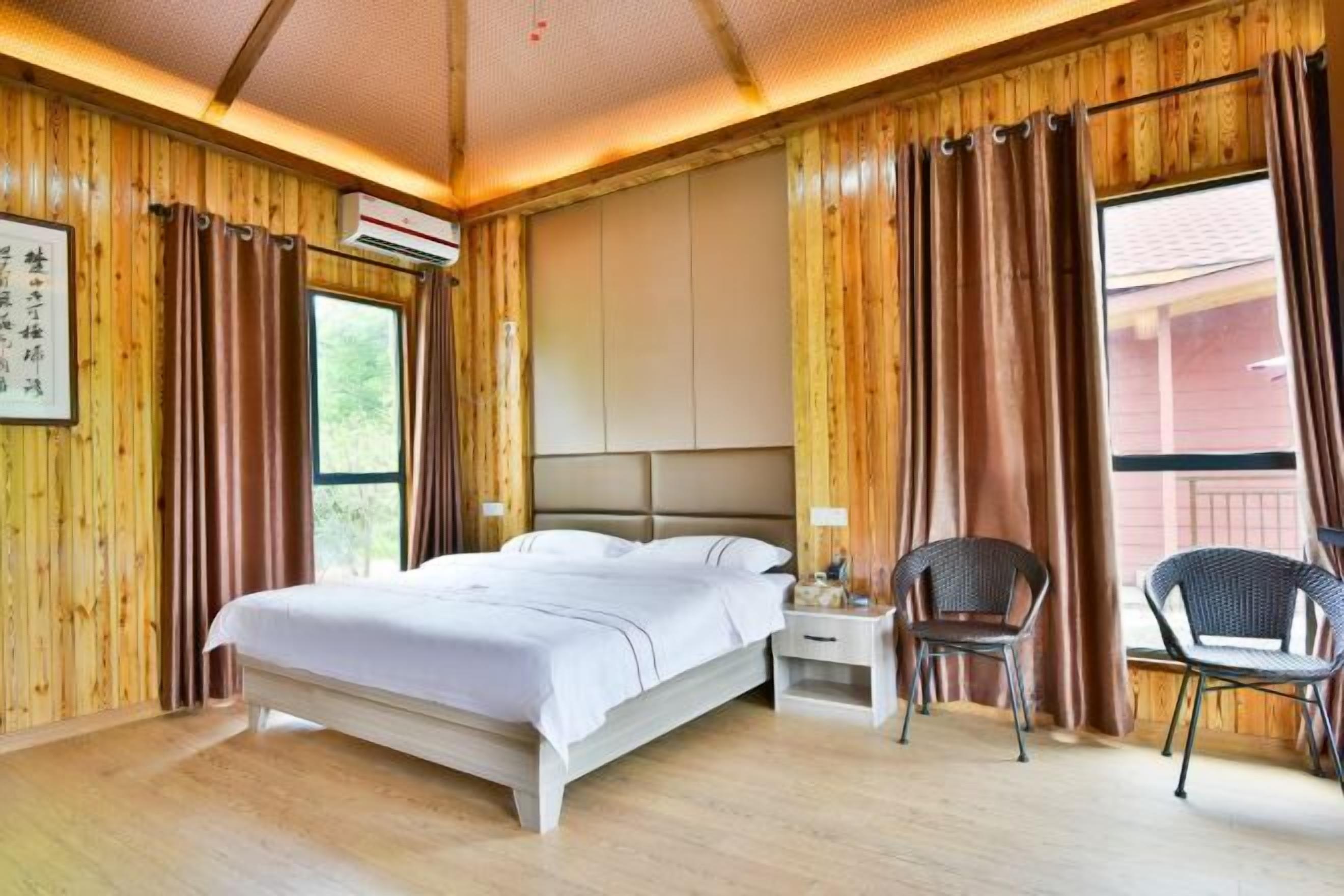Een slaapkamer met houten lambrisering, een bed, twee nachtkastjes en twee rieten stoelen.