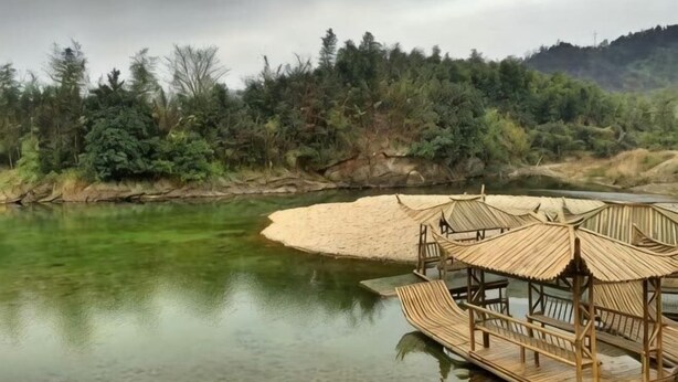 Un muelle de madera que se adentra en un río, con un pabellón de techo de paja.