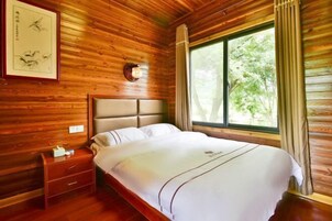 Una habitación con paneles de madera, una cama, una mesita de noche, una obra de arte enmarcada y una ventana con cortinas.