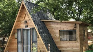 Una cabaña tipo A de madera, con techo inclinado, una puerta principal y una ventana.