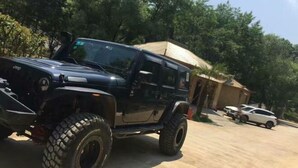 Un vehículo todoterreno negro estacionado en una entrada de casa, con una vivienda y árboles al fondo.