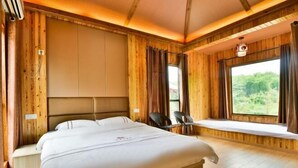 Una habitación de madera con una cama, un rincón con asiento junto a la ventana y vistas a zonas verdes.