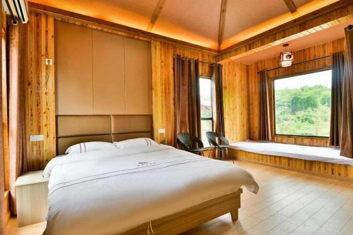 Una habitación de madera con una cama, un rincón con asiento junto a la ventana y vistas a zonas verdes.