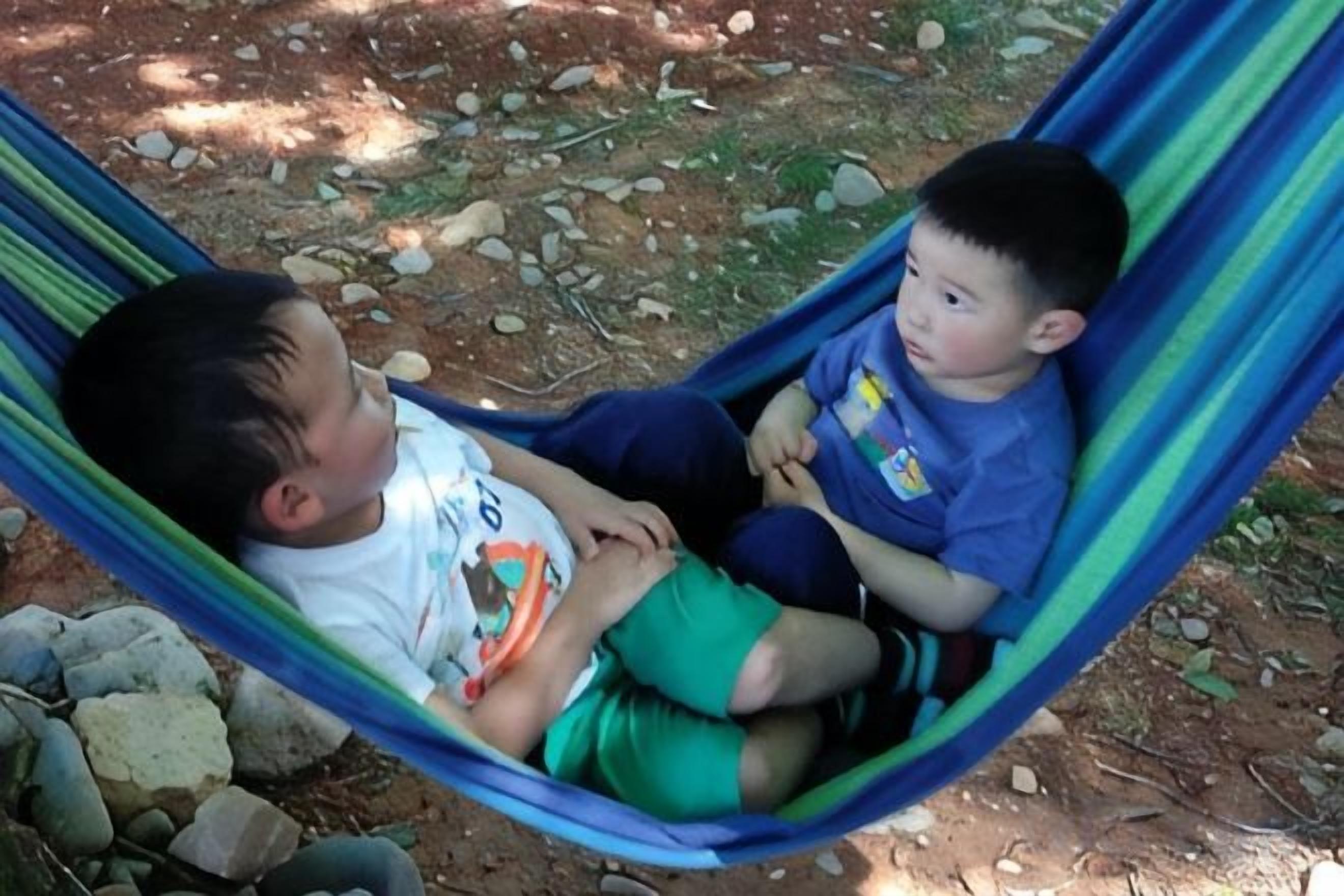 Deux enfants sont assis dans un hamac, à l’extérieur.