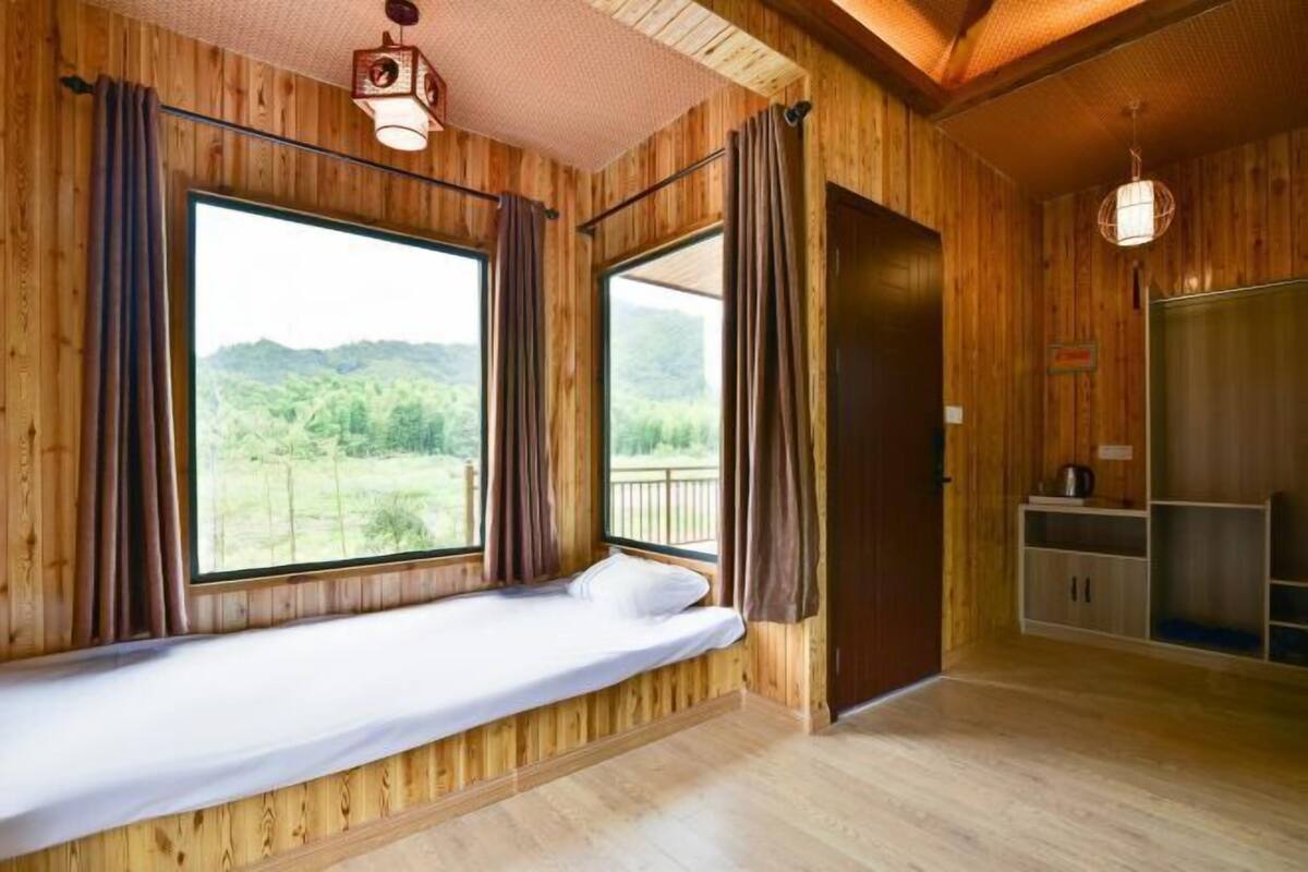 A wooden cabin with a bed, large windows, and a view of the outdoors.