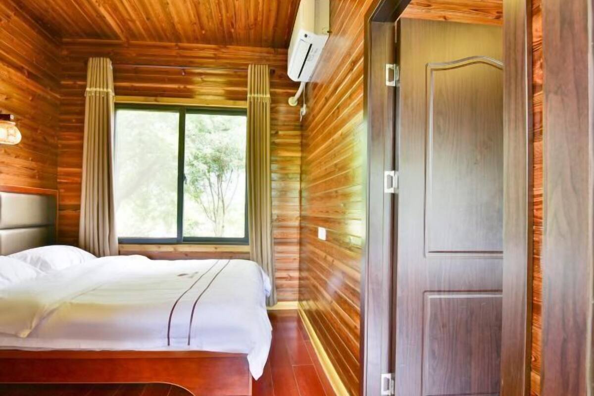 A wooden cabin room with a bed, a window, and a door.