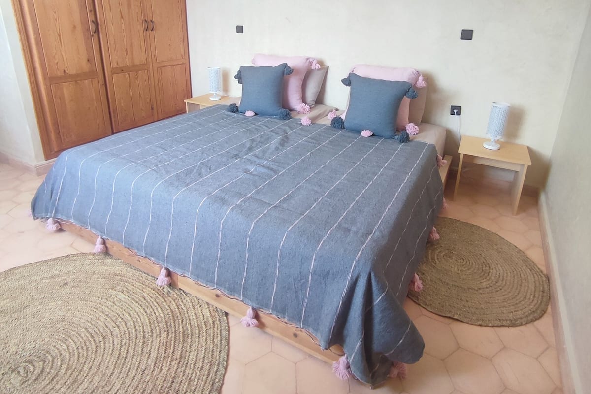 A bedroom with a large bed, two nightstands, a wooden wardrobe, and a hexagonal tiled floor.