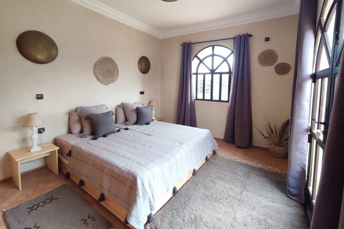 A bedroom with a large bed, bedside tables, a window with curtains, and decorative wall plates.