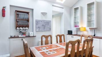A compact kitchen with a dining table, chairs, a map on the wall, and a shelf with glassware.