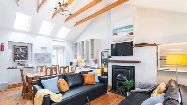 Ein modernes Wohnzimmer mit Kamin, Holzbalken und einem Essbereich mit Tisch und Stühlen.