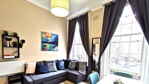 A modern living room with a sectional sofa, a dining table, and a large window with curtains. - Great Central Location 1BED APT Off OConnell ST (Dublin 1)