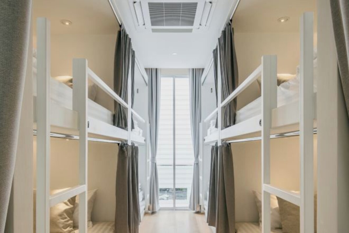 A corridor with bunk beds on either side, a large window at the end, and a ceiling fan.